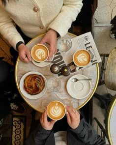 two people sitting at a table with cups of coffee in front of them and one person holding a plate