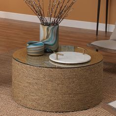 a round coffee table with a vase on top and some branches in the middle sitting on a rug