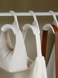 three purses hanging on a rack in a closet, one white and the other brown