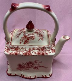 a red and white tea pot with handle on a pink tableclothed cloth background