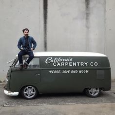 a man sitting on the roof of a green and white camper van that says california carpentry co