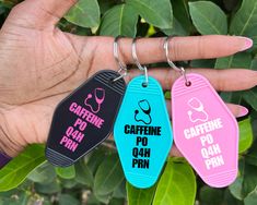 three different colored dog tags are being held by a person's hand with green leaves in the background