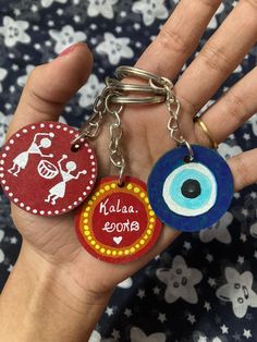 two handmade key chains with evil eye and name tags attached to them, on a person's palm