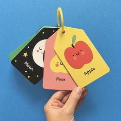 a hand holding two tags with an apple and moon on them