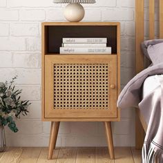 a bedside table with a lamp and books on it next to a bed in front of a white brick wall