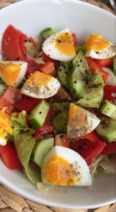 a salad with hard boiled eggs, tomatoes and cucumber in a white bowl