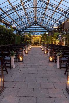 an outdoor wedding venue with lit candles and greenery on the side walk, surrounded by glass roofing