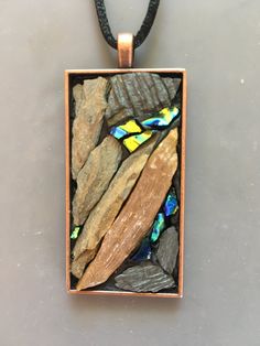 a square pendant with glass and wood in the center on a black cord necklace that is attached to a gray surface