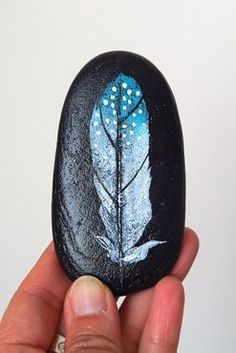 a hand holding a rock with a painted feather on it