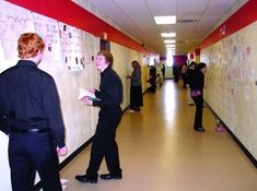 several people are standing in an office hallway and looking at notes on the wall behind them