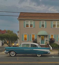 an old car is parked in front of a house with blue shutters on the windows