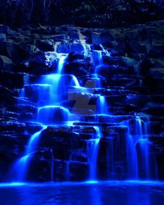 a waterfall lit up with blue lights in the night sky and water flowing down it