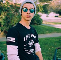 a young man wearing sunglasses and a hat standing in front of a bike with an american flag on it