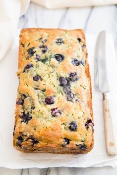 a loaf of blueberry bread sitting on top of a white napkin next to a knife and fork