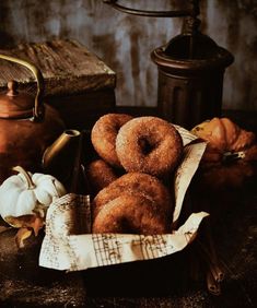 doughnuts in a basket next to a tea kettle and pumpkins on a table