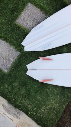 two white surfboards laying on the grass next to each other in front of a brick walkway