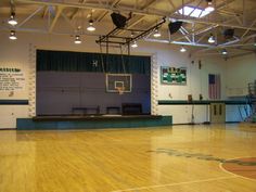 an indoor basketball court with hard wood flooring and green curtains on the side wall