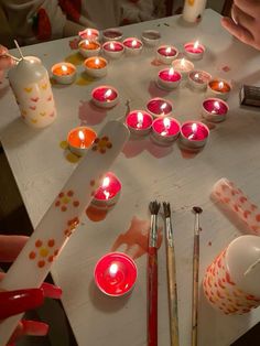 several candles are lit on a table with paintbrushes and other crafting supplies