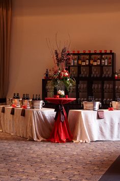 a banquet table set up with red and white linens, wine bottles on the wall