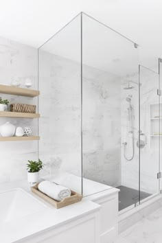 a white bathroom with glass shower doors and shelves on the wall next to the bathtub