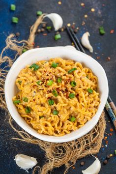 a white bowl filled with noodles and topped with chopped green onions next to chopsticks