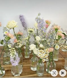 there are many different vases with flowers in them on the wooden table next to each other