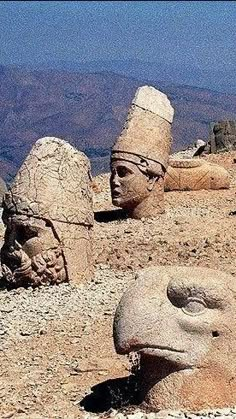 some very big statues in the middle of a desert area with mountains in the background