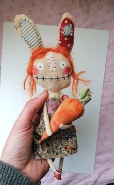 a hand holding a doll with an orange hair and carrot in it's left hand