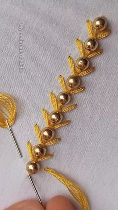 a hand holding a knitting needle with gold beads on it's end and two pins in the middle