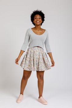 a woman standing in front of a white background wearing a gray sweater and floral print skirt