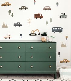 a green dresser sitting in front of a wall with cars and trucks painted on it