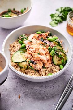 a white bowl filled with rice, cucumbers and meat next to chopsticks