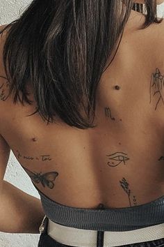 the back of a woman with tattoos on her upper and lower body, standing in front of a white wall