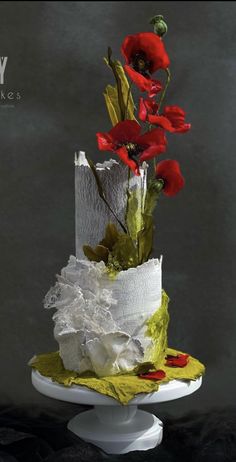 a three tiered cake with red flowers on top and white paper in the middle