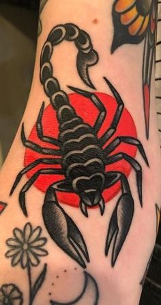 a black and red scorpion tattoo on the left arm with flowers in front of it