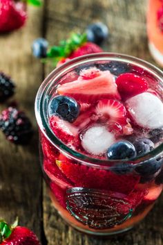 a jar filled with fruit and ice on top of a wooden table next to berries