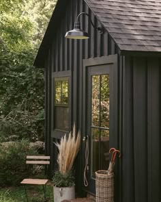 a black shed with an umbrella and some plants on the front door, next to a bench