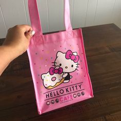 a pink hello kitty bag sitting on top of a wooden table next to a person's hand