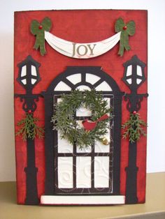 a red and black card with a wreath on it that says joy over the front door