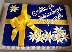 a blue and yellow birthday cake with white flowers on the bottom, and gold ribbon