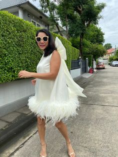 a woman in a white dress and sunglasses is standing on the sidewalk with her arms out