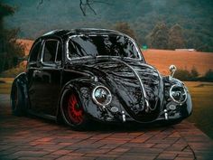 a black vw bug parked on top of a brick road next to a tree