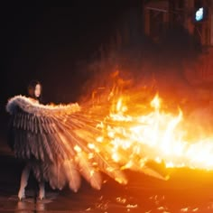 a woman standing in front of a fire with her arms spread wide and wings outstretched