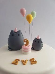 a white cake topped with two cats and balloons