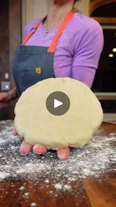 a person holding a doughnut on top of a wooden table with flour all over it