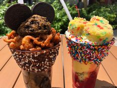 two cups filled with ice cream and desserts on top of a wooden table next to each other