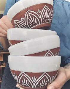 a person holding three brown and white bowls with designs on them, in their hands