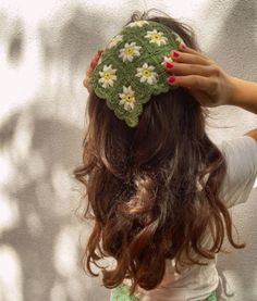 a woman with long hair wearing a crochet hat and holding her hands to her head