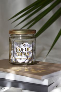 a jar of white flowers sitting on top of a book next to a palm tree