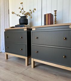 two black dressers with wooden handles and drawers on top of each other in front of a white wall